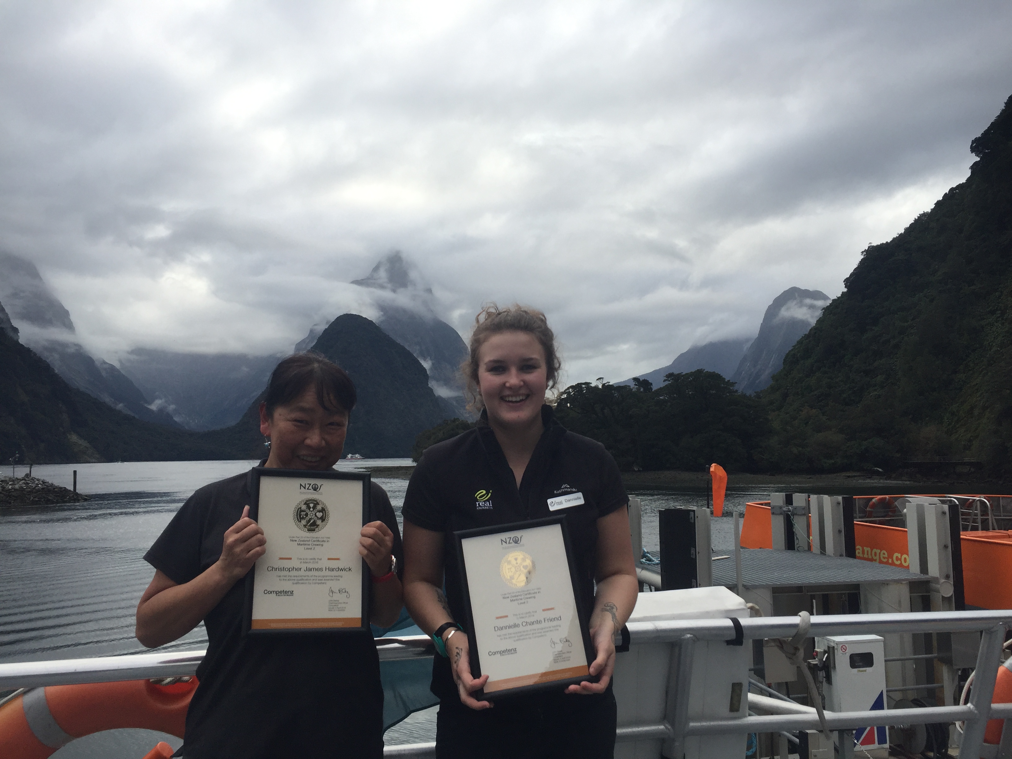 Two Real Journeys staff members holding awards in Milford Sound