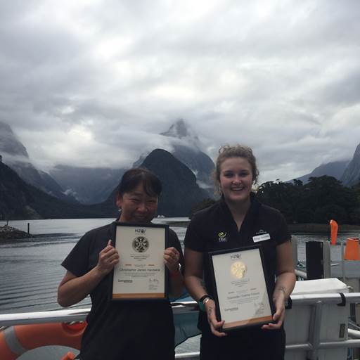 Two Real Journeys staff members holding awards in Milford Sound